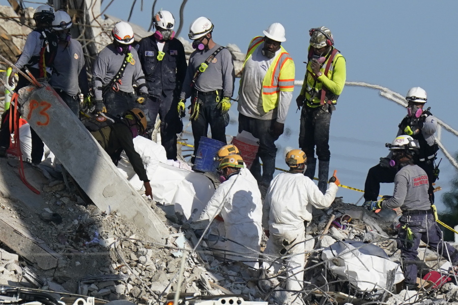 A team secures sets of recovered remains in body bags, as search and rescue personnel work atop the rubble at the Champlain Towers South condo building where scores of people remain missing more than a week after it partially collapsed, Friday, July 2, 2021, in Surfside, Fla.