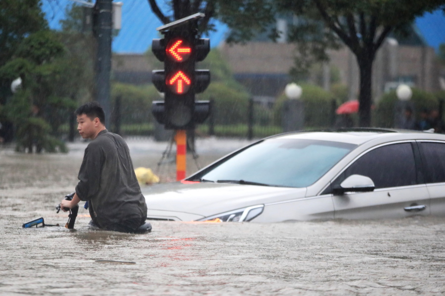 A man rides a bicycle through a flooded intersection in Zhengzhou in central China's Henan Province, Tuesday, July 20, 2021. China's military has blasted a dam to release floodwaters threatening one of its most heavily populated provinces. The operation late Tuesday night in the city of Luoyang came after several people died in severe flooding in the Henan provincial capital of Zhengzhou, where residents were trapped in the subway system and left stranded at schools, apartments and offices.