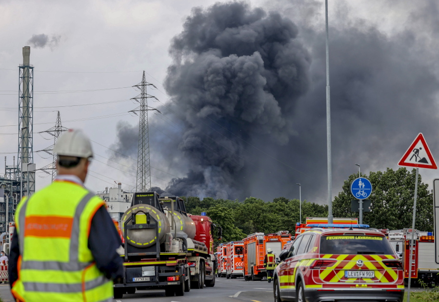 Emergency vehicles of the fire brigade, rescue services and police stand not far from an access road to the Chempark over which a dark cloud of smoke is rising in Leverkusen, Germany, Tuesday, July 27, 2021.. After an explosion, fire brigade, rescue services and police are currently in large-scale operation, the police explained.