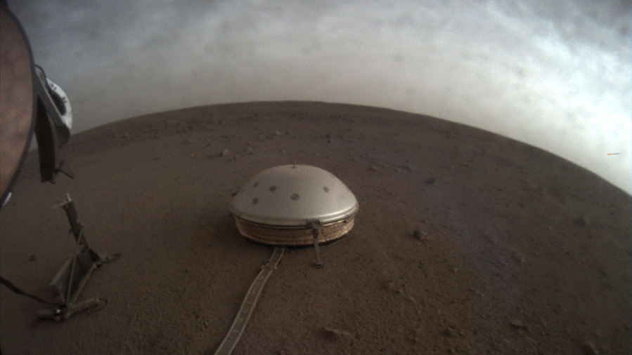 In this undated photo made available by NASA on Thursday,  July 22, 2021, clouds drift over the dome-covered SEIS seismometer of the InSight lander on the surface of Mars. The quake-measuring device is providing the first detailed look at the red planet's interior, revealing a surprisingly thin crust and a molten core. In a series of articles published in July 2021, scientists reported that the Martian crust is within the thickness range of Earth's. Mars' mantle, meanwhile, is roughly half that of our own much bigger planet, while the core -- measured from the dusty surface to dead center -- is more than 1,000 miles smaller.