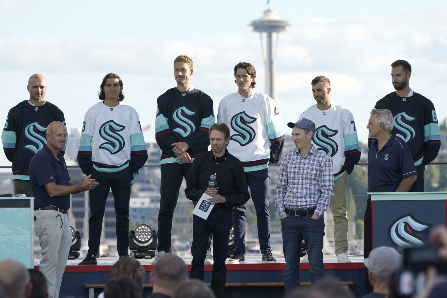 New Seattle Kraken NHL hockey players, back row from left, Mark Giordano, Brandon Tanev, Jamie Oleksiak, Hadyn Fluery, Jordan Eberle and Chris Dreidger stand on stage with Kraken owners David Wright, front left, Jerry Bruckheimer, front center, and Andy Jassy, front second from right, and Kraken general manager Ron Francis, front right, Wednesday, July 21, 2021, after being introduced during the Kraken's expansion draft event in Seattle. Jassy is also president and CEO of Amazon.com. (AP Photo/Ted S.