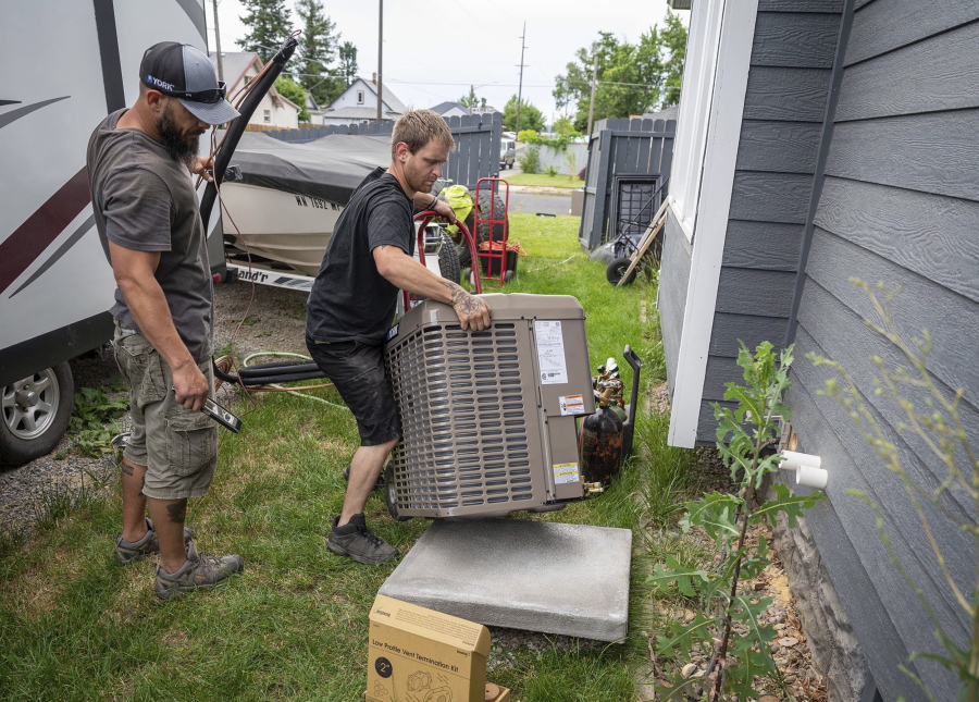 Carl Rocha, left, and Patrick Plummer, with Bills Heating & A/C Install air conditioning and a new furnace at a home on East Wabash Street, Wednesday, June 23, 2021, in Spokane, Wash. With temperatures forecast to hit over 100 degrees by Sunday, a rush of customers are keeping local A/C installers busy.