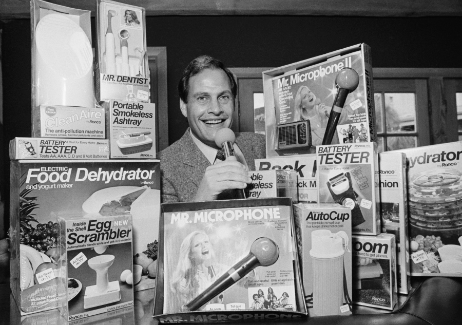 FILE - In this Wednesday, Dec. 8, 1982 file photo, Ron Popeil, the man behind those late-night, rapid-fire television commercials that sell everything from the Mr. Microphone to the Pocket Fisherman to the classic Veg-a-Matic, sits surrounded by his wares in his office in Beverly Hills, Calif.  Ron Popeil, the quintessential TV pitchman and inventor known to generations of viewers for hawking products including the Veg-O-Matic, the Chop-O-Matic, Mr. Microphone and the Showtime Rotisserie and BBQ, died Wednesday, July 28, 2021 his family said.