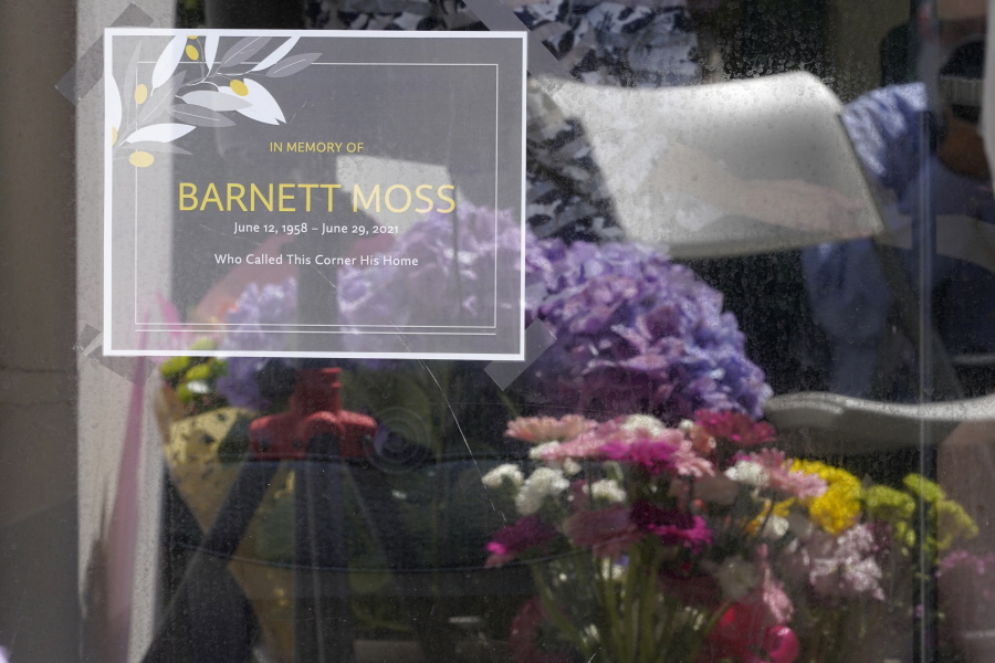 A sign noting the death of Barnett Moss is displayed as memorial flowers are reflected in the window during a memorial service for Moss -- who died last week during the Pacific Northwest Heatwave -- on the front porch entryway of the United Churches of Olympia, Friday, July 9, 2021, in Olympia, Wash. Moss slept nightly on the cement in front of the church and during the day could usually be found reading books on a bench inside the Capitol Rotunda in front of the Washington Legislature House chambers. (AP Photo/Ted S.
