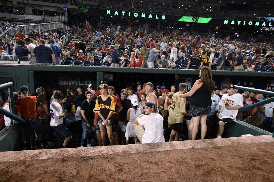 Spectators stand in the visiting team dugout during a stoppage in play due to an incident near the ballpark in the sixth inning of a baseball game between the Washington Nationals and the San Diego Padres, Saturday, July 17, 2021, in Washington.