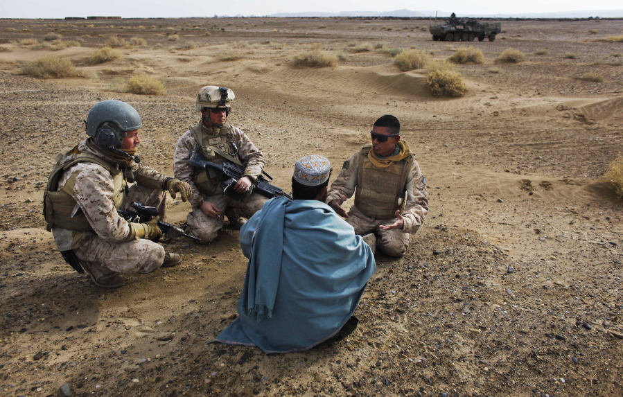 FILE - In this Friday, Dec. 11, 2009, file photo, United States Marine Sgt. Isaac Tate, left, and Cpl. Aleksander Aleksandrov, center, interview a local Afghan man with the help of a translator from the 2nd MEB, 4th Light Armored Reconnaissance Battalion on a patrol in the volatile Helmand province of southern Afghanistan. More than 200 Afghans were due to land Friday in the United States in the first of several planned evacuation flights for former translators and others as the U.S. ends its nearly 20-year war in Afghanistan.