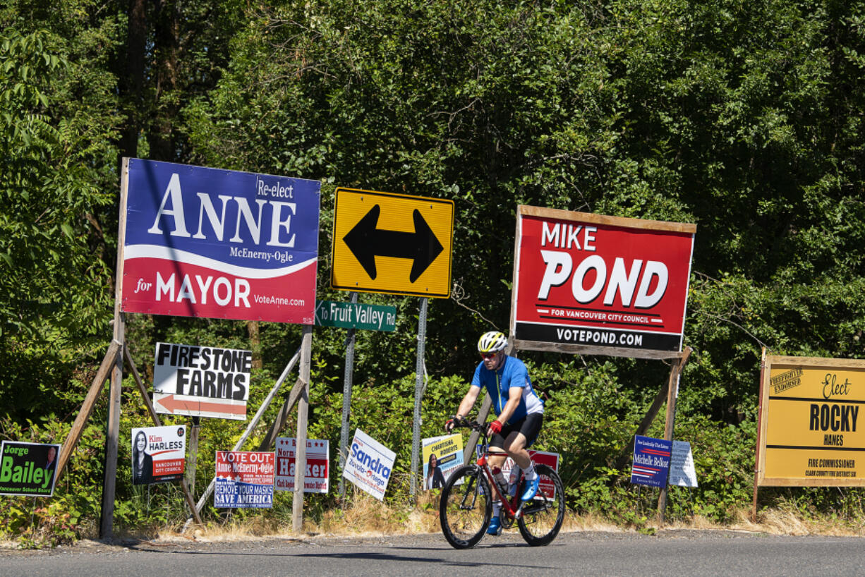 A cyclist passes signs for the upcoming election along Northwest Lakeshore Avenue on the afternoon of July 22.