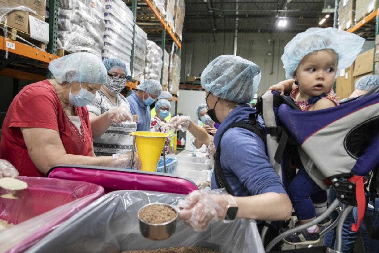 Volunteer Elyce Naray, right, carries her 1-year-old daughter, Elowen, on her back, as she helps package jambalaya meals at the Clark County Food Bank in Vancouver on Saturday. A $15,000 grant from The Church of Jesus Christ of Latter-day Saints to U.S. Hunger covered the cost of the food and packaging materials.