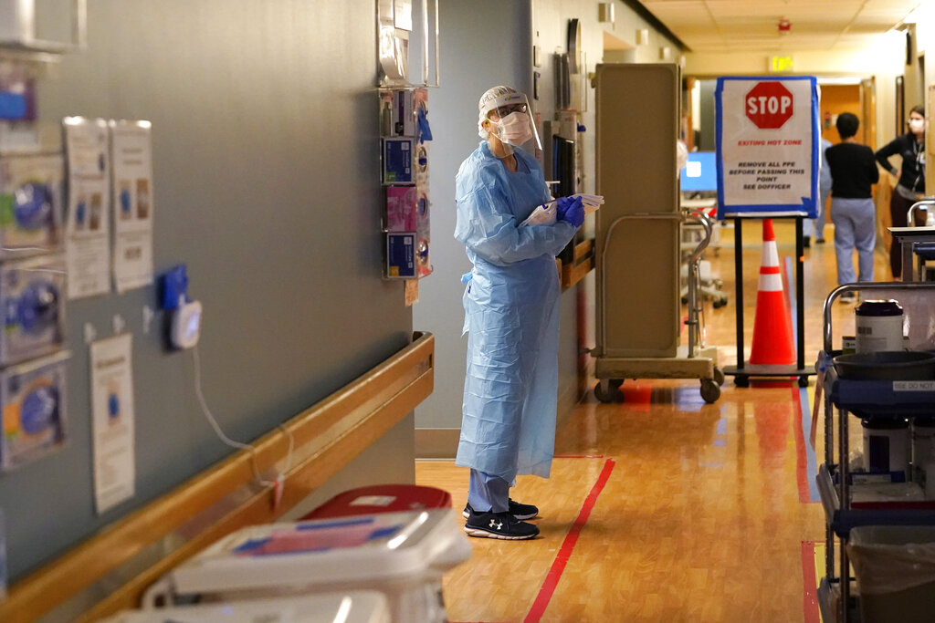 Registered nurse Diane Miller stands in the "hot zone," defined by red tape on the floor, as she waits to exchange equipment with a colleague who will remain on the other side of the tape in the COVID acute care unit at UW Medical Center-Montlake, Tuesday, Jan. 26, 2021, in Seattle. King County, where the hospital is located, has been on a downward trend of COVID-19 cases after two-and-a-half straight months of increases. But the current lull could be, and some experts believe will be, upended as more contagious variants of the virus spread throughout United States.