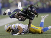 Seattle Seahawks running back Alex Collins dives over Los Angeles Chargers safety Ben DeLuca as he carries the ball during the second half of an NFL football preseason game, Saturday, Aug. 28, 2021, in Seattle.