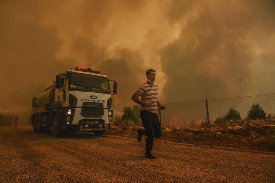 A man runs, in the fire-devastating Sirtkoy village, near Manavgat, Antalya, Turkey, Sunday, Aug. 1, 2021. More than 100 wildfires have been brought under control in Turkey, according to officials. The forestry minister tweeted that five fires are continuing in the tourist destinations of Antalya and Mugla.