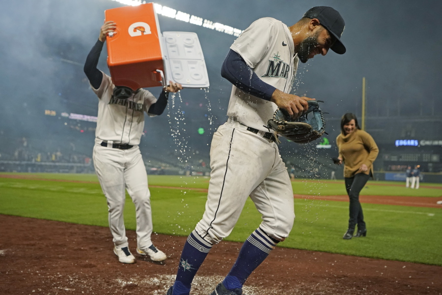 Seattle Mariners' Abraham Toro, center, has a cooler of water dumped on him by teammate Luis Torrens, left, as Toro takes part in an interview after the team's baseball game against the Houston Astros, Tuesday, Aug. 31, 2021, in Seattle. Toro hit a grand slam in the eighth inning to give the Mariners a 4-0 win. (AP Photo/Ted S.