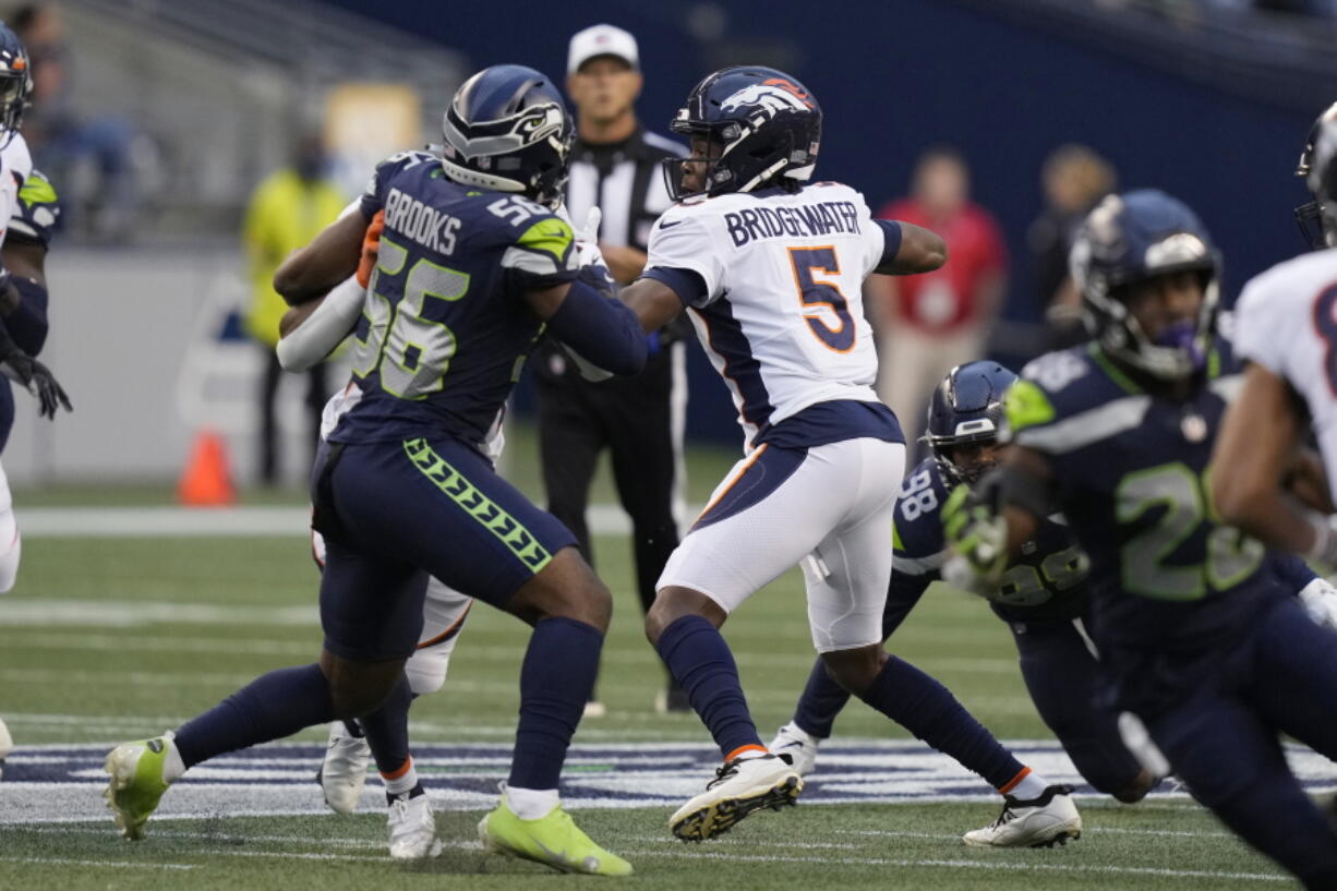 Denver Broncos quarterback Teddy Bridgewater (5) looks for a receiver while under pressure from Seattle Seahawks linebacker Jordyn Brooks (56) during the first half of an NFL preseason football game Saturday, Aug. 21, 2021, in Seattle.