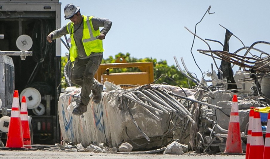 A worker jumps off a large piece of rubble on the site of the Champlain Towers South collapse, in Surfside, Fla., Monday, July 19, 2021. Two close friends and former New Yorkers are among the last of the missing as the South Florida condo search stretches into a fourth week.