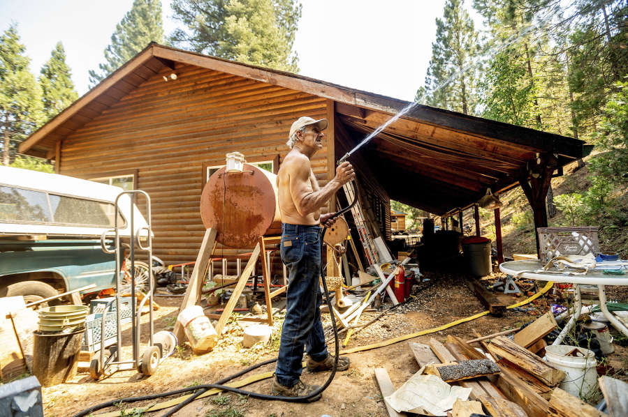 Dan Santos sprays water while defending his girlfriend's Greenville home as the Dixie Fire burns nearby in Plumas County, Calif., on Tuesday, Aug. 3, 2021. Dry and windy conditions have led to increased fire activity as firefighters battle the blaze which ignited July 14.