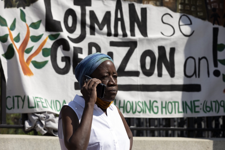 A woman speaks on the phone in front of a sign in Haitian Creole during a news conference held by a coalition of housing justice groups to protest evictions, Friday, July 30, 2021, outside the Statehouse in Boston.