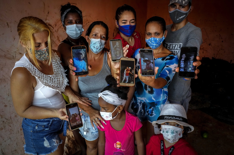 Zuleydis "Zuly" Elledias, left, shows a cellphone photo of her missing husband to a child while her neighbors pose for a group picture holding up cellphone photos of their missing relatives who ventured out in homemade boats in an attempt to reach Florida, in Orlando Nodarse, about 60 kilometers west of Havana, Cuba, Wednesday, June 30, 2021. Cuba is seeing a surge in unauthorized migration to the United States, fueled by an economic crisis.