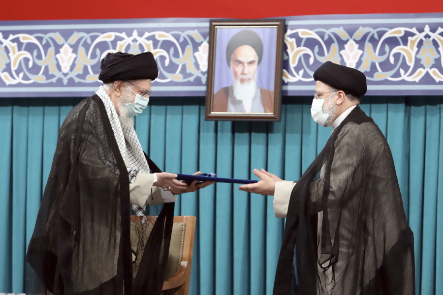 In this photo released by an official website of the office of the Iranian supreme leader, Supreme Leader Ayatollah Ali Khamenei, left, gives his official seal of approval to newly elected President Ebrahim Raisi in an endorsement ceremony in Tehran, Iran, Tuesday, Aug. 3, 2021. A portrait of the late revolutionary founder Ayatollah Khomeini hangs in the background.