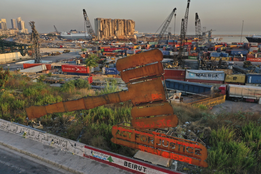 A justice symbol monument is seen in front of towering grain silos that were gutted in the massive August 2020 explosion at the port that claimed the lives of more than 200 people, in Beirut, Lebanon, Wednesday, Aug. 4, 2021. A year after the deadly blast, families of the victims are consumed with winning justice for their loved ones and punishing Lebanon's political elite, blamed for causing the disaster through their corruption and neglect.