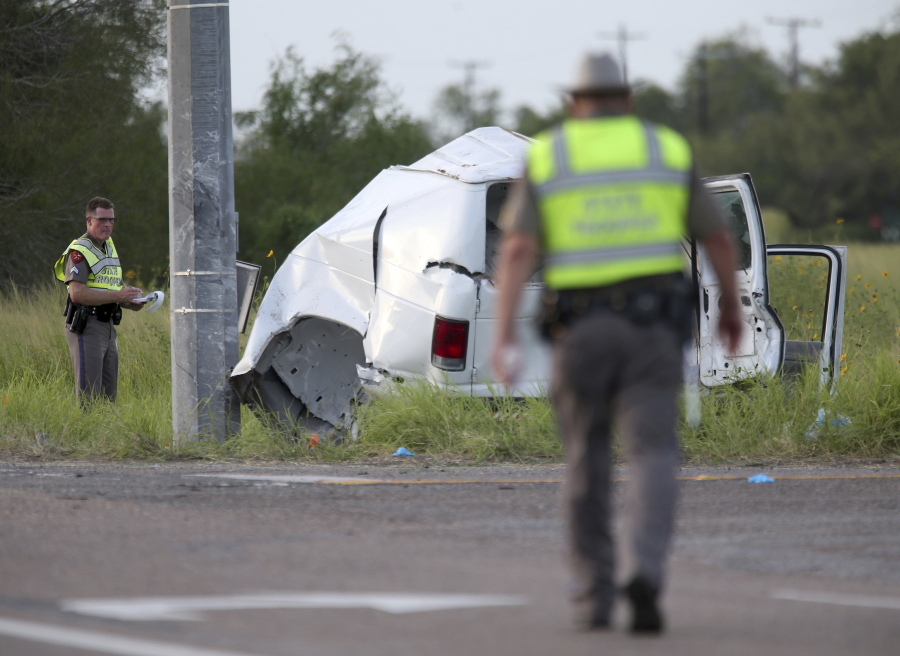 Texas Department of Public Safety officers pick up debris near a vehicle where multiple people died after the van carrying migrants tipped over just south of the Brooks County community of Encino on Wednesday, Aug. 4, 2021, in Encino, Texas. The van crashed against a utility pole after it attempted to turn off of Highway 281 onto Business 281. Encino is about 2 miles (3.22 kilometers) south of the Falfurrias Border Patrol checkpoint.
