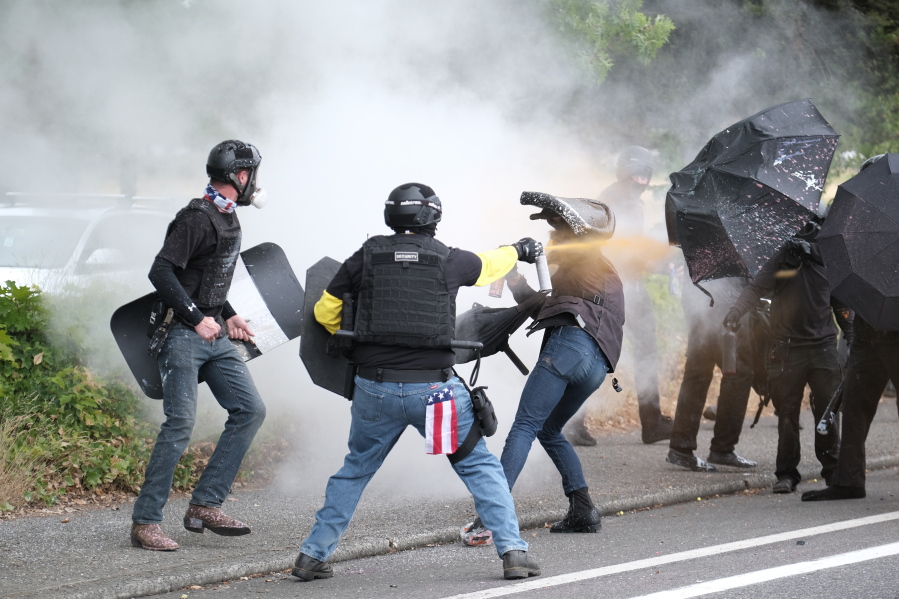 This Sunday, Aug. 22, 2021 photo, members of the far-right group Proud Boys and anti-fascist protesters spray bear mace at each other during clashes between the politically opposed groups in Portland, Ore.  Police in Portland have been criticized that they did little to prevent violent clashes between right- and left-wing protesters on Sunday.