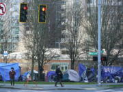 FILE - In this March 3, 2021, file photo, with apartment buildings in the background, pedestrians walk past tents used by people lacking housing at Denny Park near the Space Needle in Seattle. A Washington state judge on Friday, Aug. 27, 2021, struck a Seattle measure on homelessness from the November ballot even as the city remains mired in a long-term humanitarian crisis. (AP Photo/Ted S.