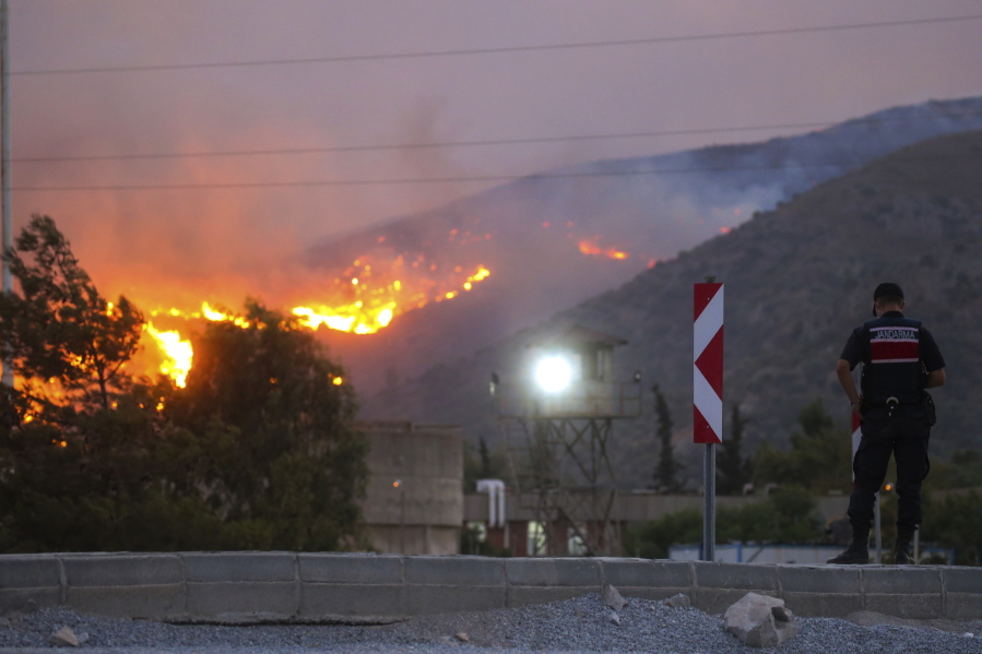 A paramilitary police officer stands close to Kemerkoy Thermal Power Plant, right, with the blaze approaching in the background, in Milas, Mugla, Turkey, Tuesday, Aug. 3, 2021. Turkish President Recep Tayyip Erdogan's government is facing increased criticism over its apparent poor response and inadequate preparedness for large-scale wildfires that have left eight people dead and forced thousands to flee their homes.