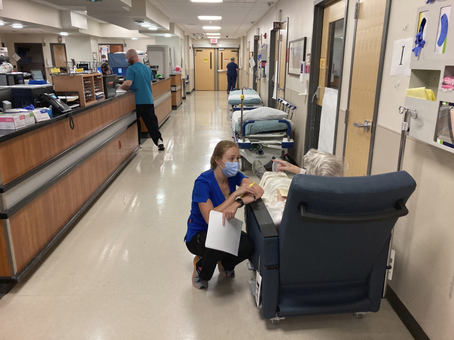 FILE - In this Aug. 20, 2021, file photo, a nurse talks to a patient in the emergency room at Salem Hospital in Salem, Ore., with gurneys lining the hallway behind them, ready to take patients if needed. Gov. Kate Brown announced Wednesday, Aug. 25, 2021, that the state has contracted with a medical staffing company to provide up to 500 health care workers to hospitals around the state to help respond to the surge in patients due to the delta variant.