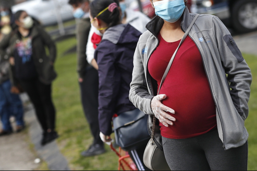FILE - In this May 7, 2020 file photo, a pregnant woman wearing a face mask and gloves holds her belly as she waits in line for groceries at St. Mary's Church in Waltham, Mass. The Centers for Disease Control and Prevention urged all pregnant women Wednesday, Aug. 11, 2021 to get the COVID-19 vaccine as hospitals in hot spots around the U.S. see disturbingly high numbers of unvaccinated mothers-to-be seriously ill with the virus.
