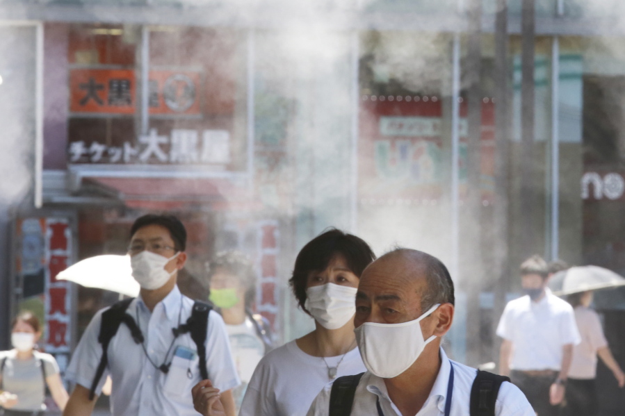 People wearing face masks to protect against the spread of the coronavirus walk under a water mist in Tokyo Thursday, Aug. 5, 2021. New cases surge in Tokyo to record levels during the Olympic Games.