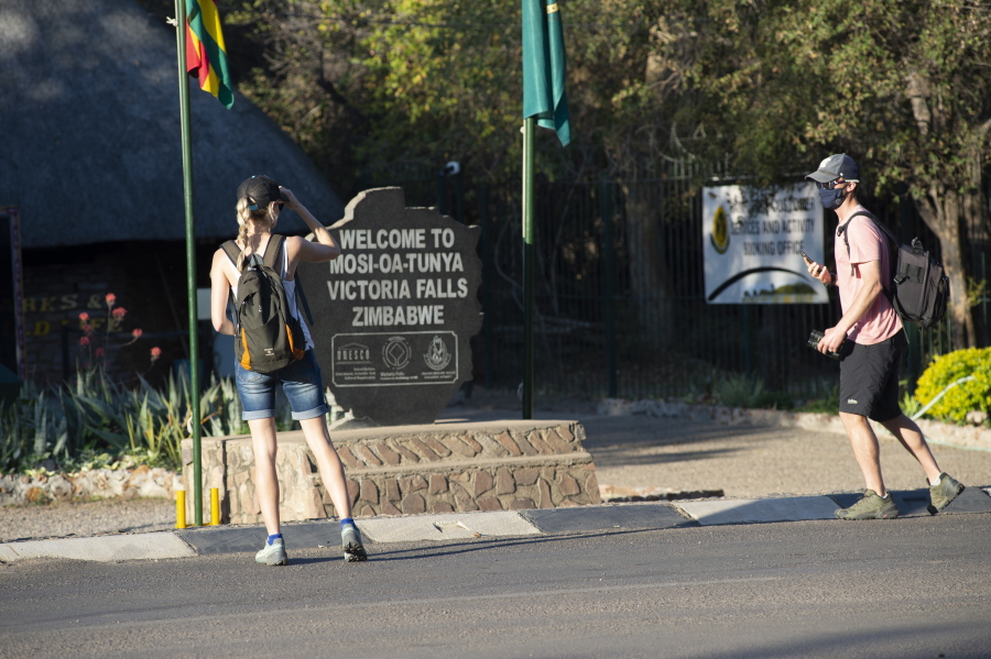 Tourists wear face masks at the entrance of the Victoria Falls in Victoria Falls in this Friday, Aug, 6, 2021 photo. To promote Victoria Falls as a safe tourist destination, President Emmerson Mnangagwa's government has made vaccinations available to all 35,000 residents of the town, and an estimated 60% of the people in Victoria Falls have now been vaccinated with either the Sinopharm or Sinovac vaccines, both from China.