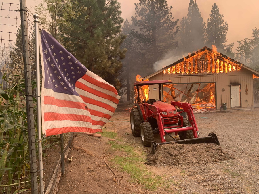 A red tractor is left behind as a home burns outside of Taylorsville in Plumas County, Calif., that was impacted by the Dixie Fire Friday, Aug. 13, 2021. The U.S. Forest Service said Friday it's operating in crisis mode, fully deploying firefighters and maxing out its support system as wildfires continue to break out across the U.S. West. The agency says it has more than twice the number of firefighters working on the ground than at this point a year ago, and is facing "critical resources limitations." An estimated 6,170 firefighters alone are battling the Dixie Fire in Northern California, the largest of 100 large fires burning in 14 states, with dozens more burning in western Canada. It has destroyed more than 1,000 structures in the northern Sierra Nevada.