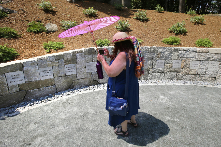 FILE - In this July 19, 2017, file photograph, Karla Hailer, a fifth-grade teacher from Scituate, Mass., shoots a video where a memorial stands at the site in Salem, Mass., where five women were hanged as witches more than 325 years earlier. A woman convicted of witchcraft in 1693 and sentenced to death at the height of the Salem Witch Trials finally will be exonerated if Massachusetts lawmakers approve a bill inspired by a curious eighth-grade history class. State Sen. Diana DiZoglio, a Democrat from Methuen, has introduced legislation to clear the name of Elizabeth Johnson Jr., 328 years after she was condemned but never executed. DiZoglio says she was inspired by sleuthing done by a group of 13- and 14-year-olds at North Andover Middle School.