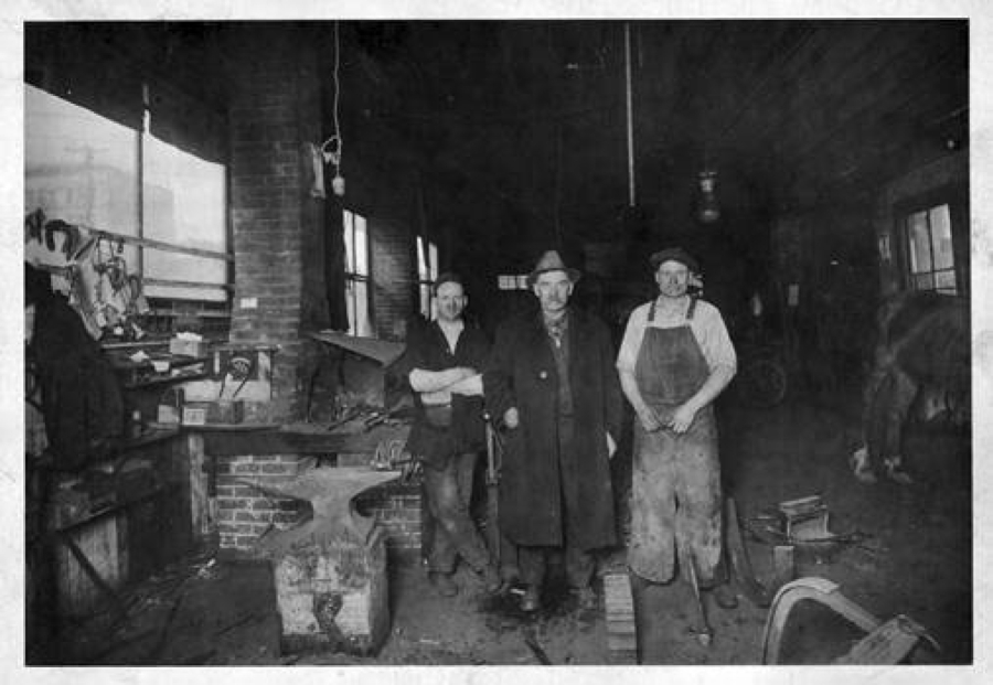 Three men inside Cooper's Blacksmith Shop at Fifth Street and Broadway in Vancouver interrupt their work to pose for a photo. From left to right: owner M.J. Cooper, J.E. Johnson and Heckman (first name unknown). In the horse-drawn era, blacksmiths forged tools, wheel rims and every tool they used. Blacksmith shops often attracted local men who chewed, smoked and exchanged gossip.