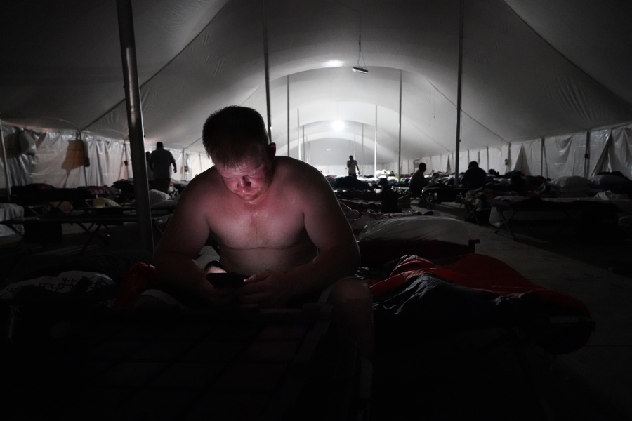Bryan Willis, of Stilwell, Okla., an electrical worker for Ozarks Electric, looks at his phone before going to bed in a tent city for electrical workers in Amelia, La., Thursday, Sept. 16, 2021. When Hurricane Ida was brewing in the Gulf of Mexico, the grass was chest high and the warehouse empty at this lot in southeastern Louisiana. Within days, electric officials transformed it into a bustling "tent city" with enormous, air-conditioned tents for workers, a gravel parking lot for bucket trucks and a station to resupply crews restoring power to the region.