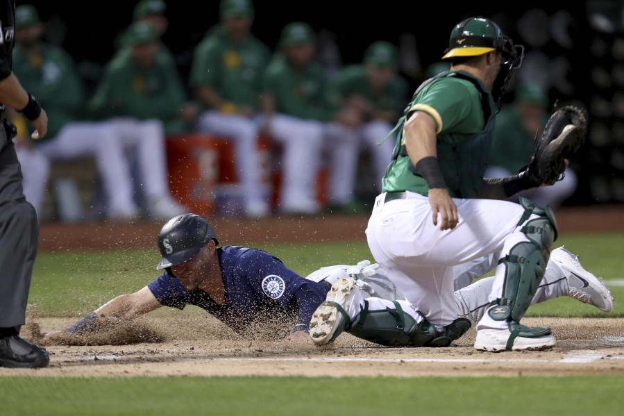 Seattle Mariners' Jake Bauers slides home safe on a throwing error by Paul Blackburn as Oakland Athletics' Yan Gomes applies the tag during the second inning of a baseball game in Oakland, Calif., Tuesday, Sept. 21, 2021.