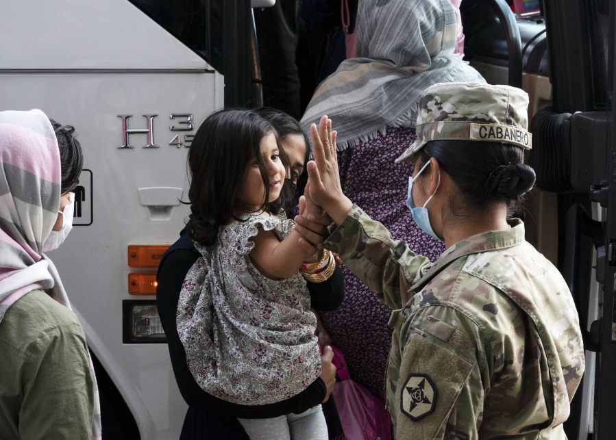 FILE - In this Monday, Aug. 30, 2021, file photo, Army Pfc. Kimberly Hernandez gives a high-five to a girl evacuated from Kabul, Afghanistan, before boarding a bus after they arrived at Washington Dulles International Airport, in Chantilly, Va. U.S. religious groups of many faiths are gearing up to assist the thousands of incoming refugees.