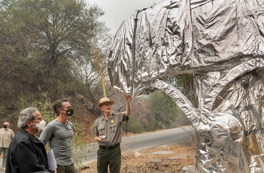 State Assembly Member Richard Bloom, D-Santa Monica, left, and California Gov. Gavin Newsom, second left, listen to Superintendent of Sequoia and Kings Canyon National Parks Clay Jordan, right, talk about the protective structure wrap used to protect the welcome sign and giant sequoia trees from the KNP Complex Fire, on Thursday, Sept. 23, 2021, in Sequoia National Park, Calif. Newsom on Thursday approved nearly $1 billion in new spending to prevent wildfires, signaling a policy shift in a state that historically focused more on putting out fires than stopping them before they start.
