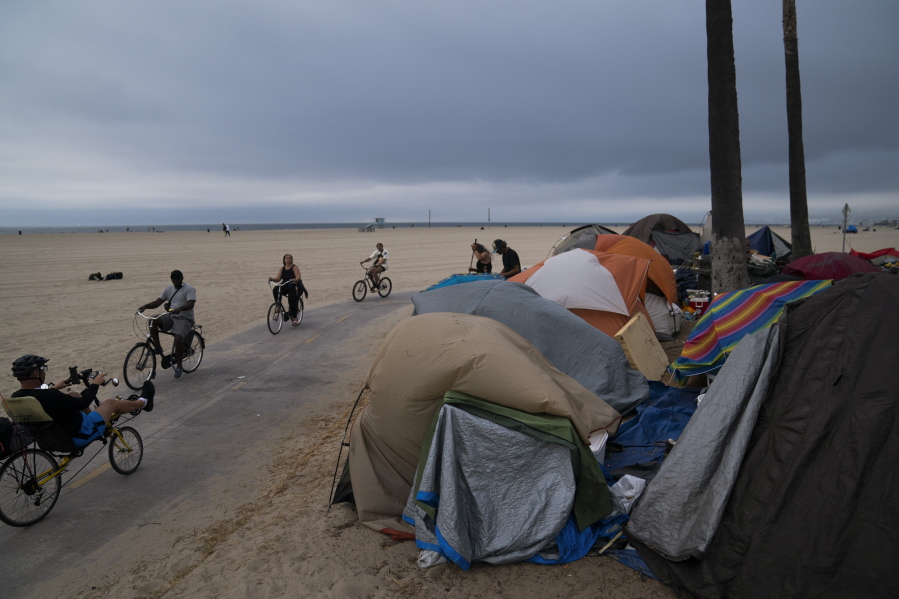 FILE - In this June 29, 2021, file photo people ride their bikes past a homeless encampment set up along the boardwalk in the Venice neighborhood of Los Angeles. The share of Americans living in poverty rose slightly as the COVID pandemic shook the economy last year, but massive relief payments pumped out by Congress eased hardship for many, the Census Bureau reported Tuesday, Sept. 14. The official poverty measure showed an increase of 1 percentage point in 2020, indicating that 11.4 percent of Americans were living in poverty. It was the first increase in poverty after five consecutive annual declines. (AP Photo/Jae C.