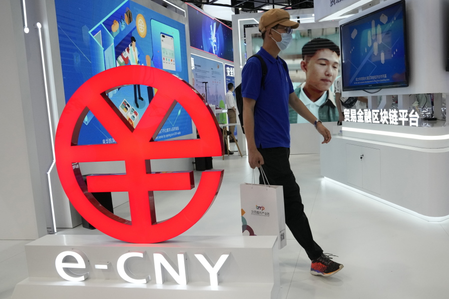 A visitor passes by a logo for the e-CNY, a digital version of the Chinese Yuan, displayed during a trade fair in Beijing, China, Sunday, Sept. 5, 2021. China's central bank on Friday, Sept. 24, 2021 declared all transactions involving Bitcoin and other virtual currencies illegal, stepping up a campaign to block use of unofficial digital money. It is developing an electronic version of the country's yuan for cashless transactions that can be tracked and controlled by Beijing.