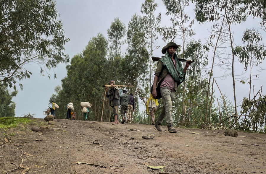 An unidentified armed militia fighter walks down a path as villagers flee with their belongings in the other direction, near the village of Chenna Teklehaymanot, in the Amhara region of northern Ethiopia Thursday, Sept. 9, 2021.