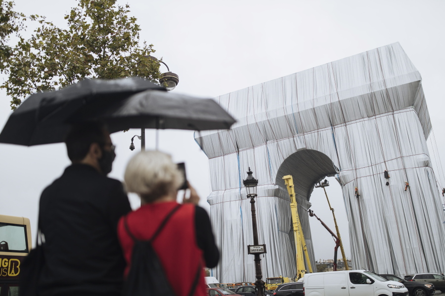 People watch workers wrapping the Arc de Triomphe monument, Wednesday, Sept. 15, 2021 in Paris. The "L'Arc de Triomphe, Wrapped" project by late artist Christo and Jeanne-Claude will be on view from, Sept. 18 to Oct. 3. The famed Paris monument will be wrapped in 25,000 square meters of fabric in silvery blue, and with 3,000 meters of red rope.