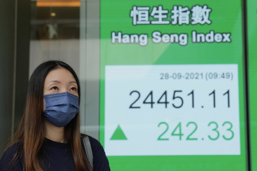 A woman wearing a face mask walks past a bank's electronic board showing the Hong Kong share index in Hong Kong, Tuesday, Sept. 28, 2021. Asian shares mostly fell Tuesday as concerns about China chipped away at investor optimism following a mixed finish on Wall Street.