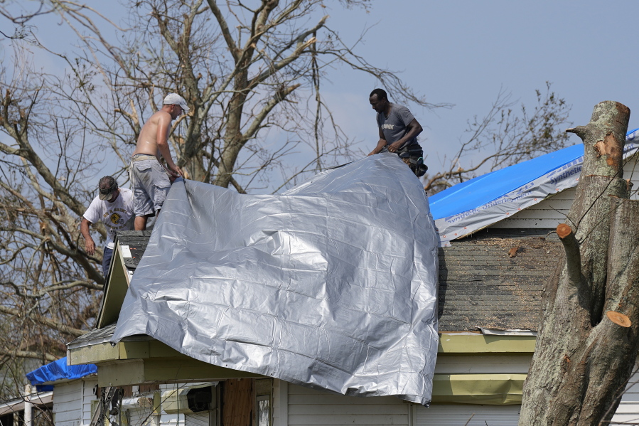 Gary Johnston, left, Grant Boughamer, center, and Jose Garcia, right, place a tarp on a roof damaged by Hurricane Ida, Thursday, Sept. 2, 2021, in Golden Meadow, La. (AP Photo/David J.