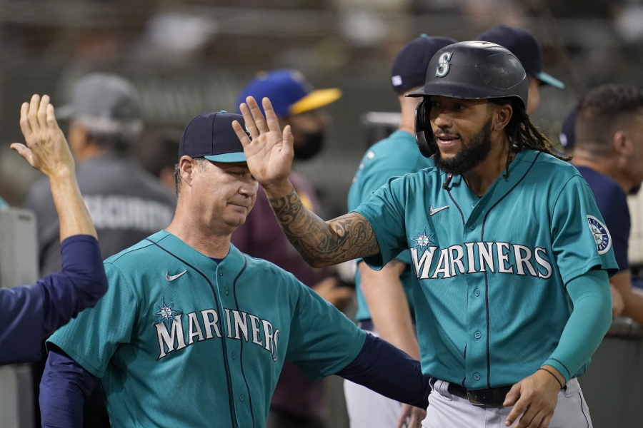 Seattle Mariners' J.P. Crawford, right, is congratulated by manager Scott Servais, left, and teammates after scoring a run against the Oakland Athletics during the third inning of a baseball game in Oakland, Calif., Monday, Sept. 20, 2021.