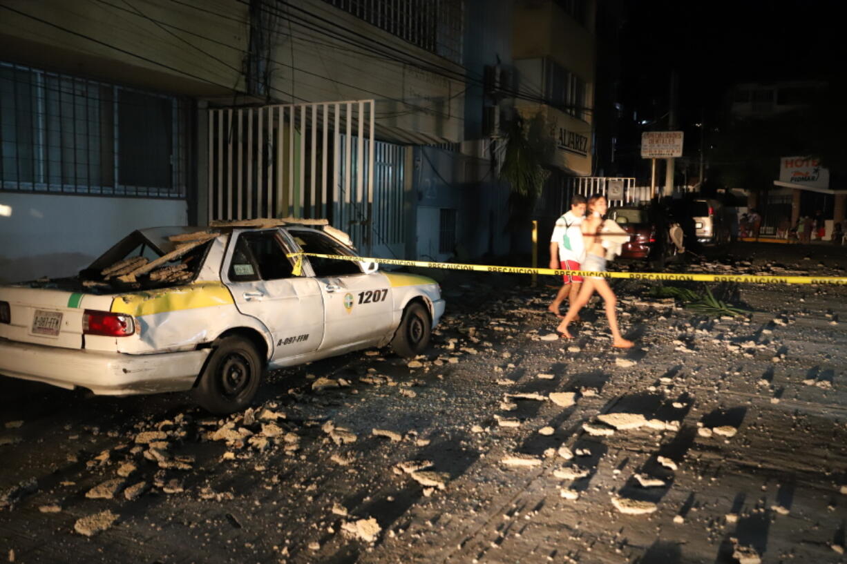 A couple walks past a taxi cab that was damaged by falling debris after a strong earthquake in Acapulco, Mexico, Tuesday, Sept. 7, 2021. The quake struck southern Mexico near the resort of Acapulco, causing buildings to rock and sway in Mexico City nearly 200 miles away.