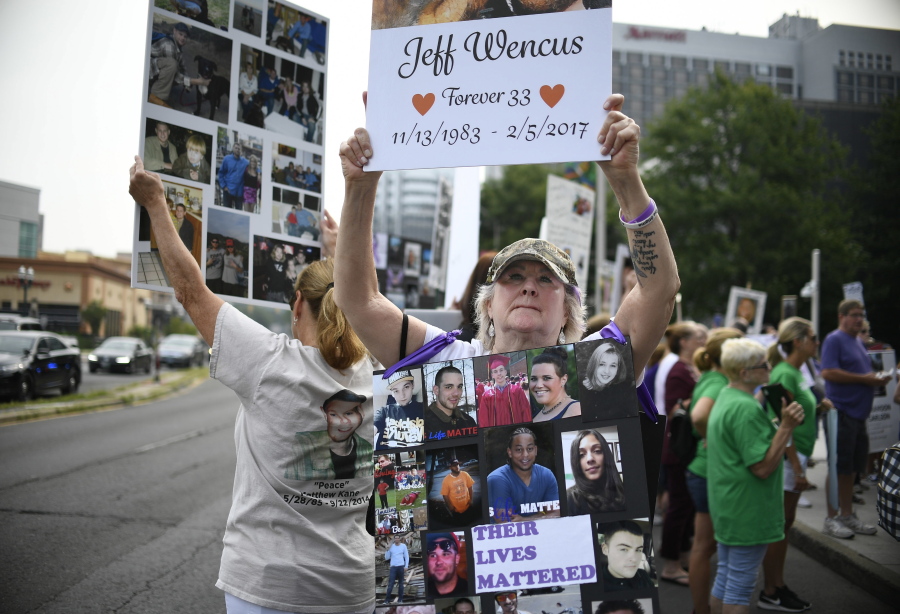 FILE - In this Aug. 17, 2018, file photo, Lynn Wencus of Wrentham, Mass., holds a sign with a picture of her son Jeff and wears a sign of others' loved ones lost to OxyContin and other opioids during a protest at Purdue Pharma LLP headquarters in Stamford, Conn. A landmark settlement in the nation's opioid epidemic is forcing the owners of OxyContin maker Purdue Pharma to give up the company and pay out $4.5 billion. "Am I happy they don't have to admit guilt and give up all their money? Of course not," said Wencus. "But what would that do?