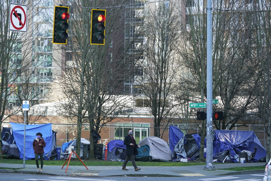 With apartment buildings in the background, pedestrians walk March 3 past tents used by people lacking housing at Denny Park near the Space Needle in Seattle. (Ted S.