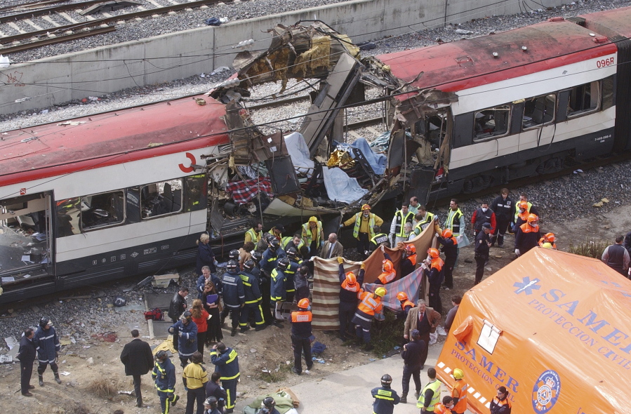 FILE - In this March 11, 2004 file photo rescue workers cover up bodies alongside a bomb-damaged passenger train, following a number of explosions in Madrid, Spain, March 11, 2004. In the 20 years since the Sept. 11, 2001 terrorist attacks in the United States, a mixture of homegrown extremists, geography and weaknesses in counterterrorism strategies have combined to turn Europe into a prime target for jihadists bent on hurting the West.