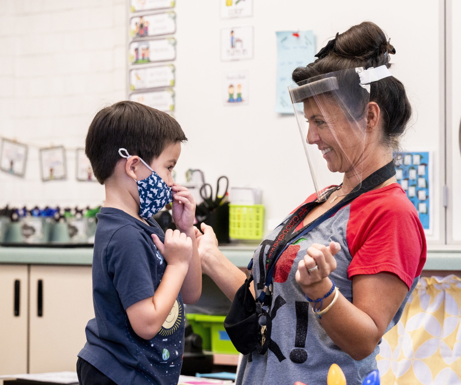 A student gets help with his mask from transitional kindergarten teacher Annette Cuccarese on Aug. 12, the first day of classes at Tustin Ranch Elementary School in Tustin, Calif. Now that California schools have welcomed students back to in-person learning, they face a new challenge: A shortage of teachers and all other staff.